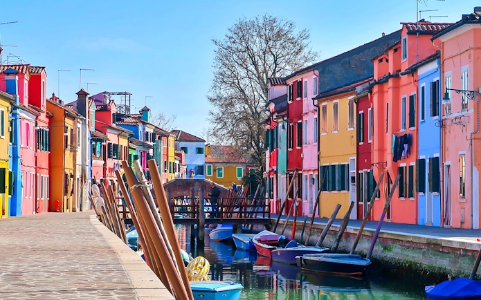 Colorful houses along a canal in Burano, Italy, with boats and a footbridge.