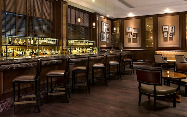 Bar area at World Cut Steakhouse, featuring a row of stools and a well-stocked bar, part of La Perle VIP experience.