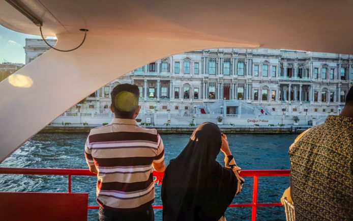 Tourists on a Bosphorus cruise viewing Dolmabahçe Palace in Istanbul.