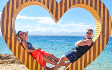 Couple relaxing in a heart-shaped frame by the sea on a High-Speed Sea Taxi Tour to Orange Bay.