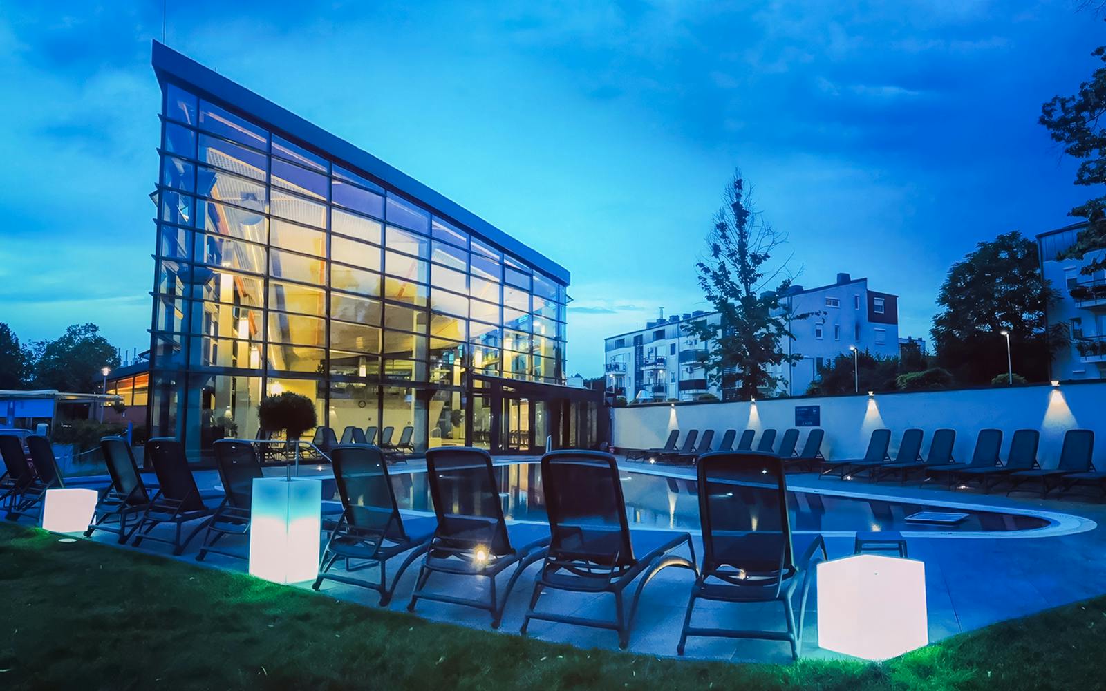 Paskal Thermal Bath in Budapest with modern glass building and poolside loungers at dusk.