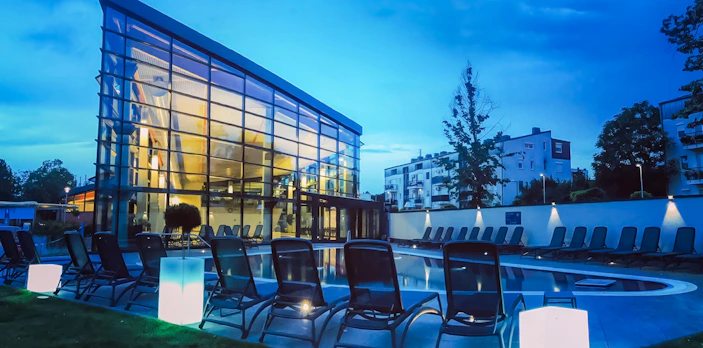 Paskal Thermal Bath in Budapest with modern glass building and poolside loungers at dusk.