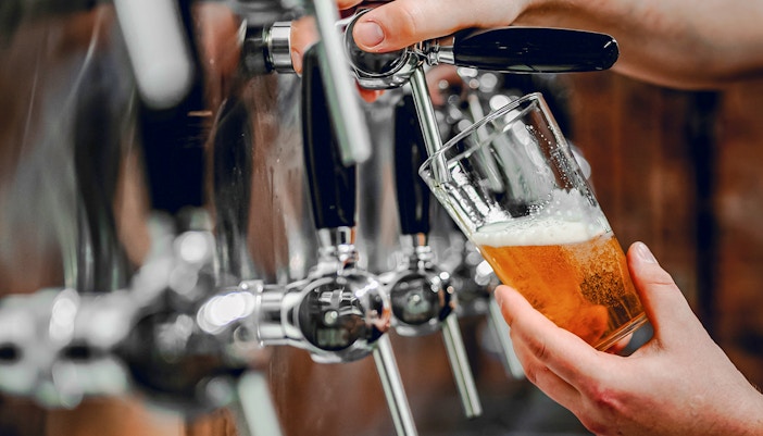 Hand pouring beer from tap into glass at a bar.