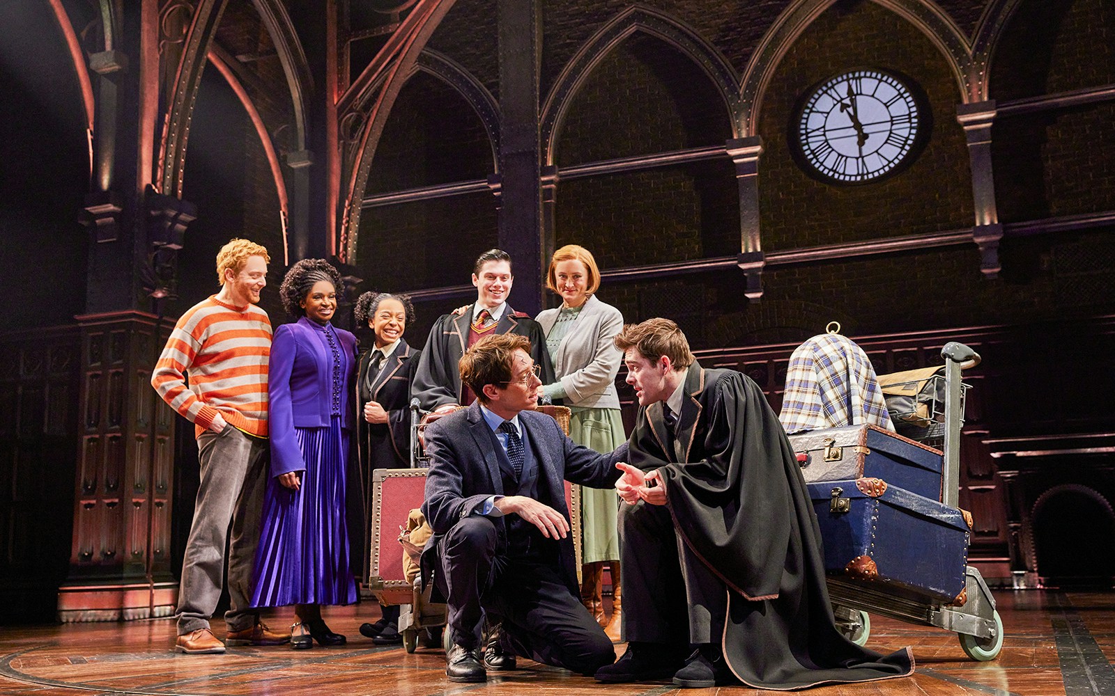 Cast of "Harry Potter and the Cursed Child" performing on stage with Hogwarts backdrop.