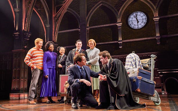 Cast of "Harry Potter and the Cursed Child" performing on stage with Hogwarts backdrop.