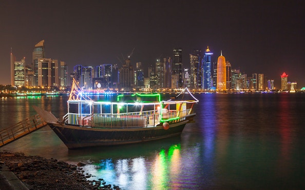 Dhow boat illuminated with lights against Doha skyline at night.