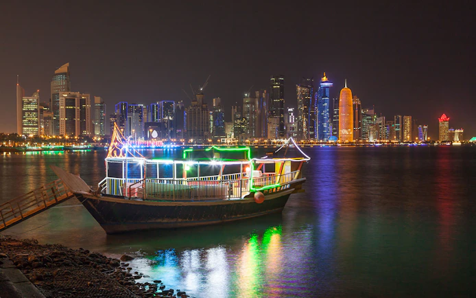 Dhow boat illuminated with lights against Doha skyline at night.