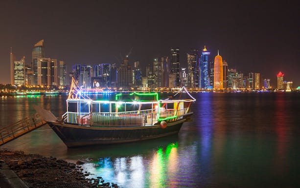Dhow boat illuminated with lights against Doha skyline at night.