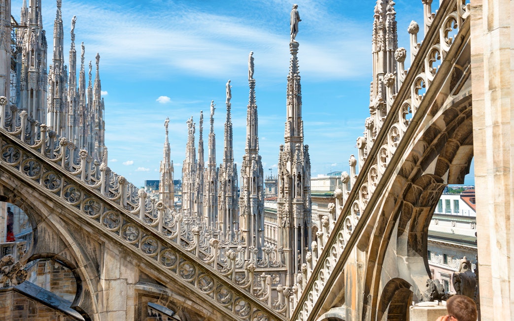 Statues atop spires of Milan Cathedral Duomo under blue sky.
