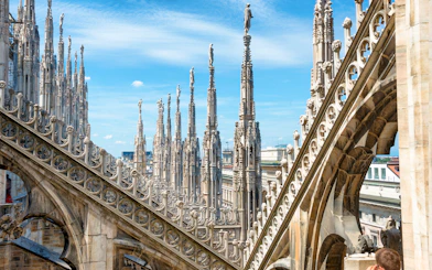 Statues atop spires of Milan Cathedral Duomo under blue sky.