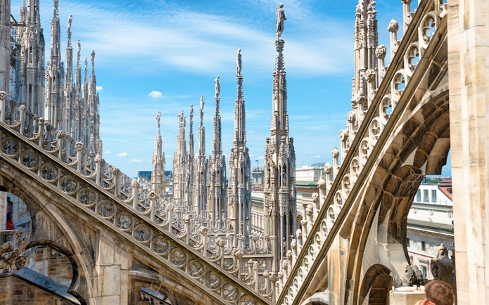 Statues atop spires of Milan Cathedral Duomo under blue sky.