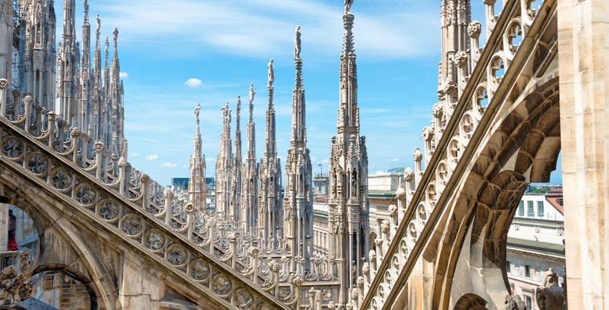Statues atop spires of Milan Cathedral Duomo under blue sky.