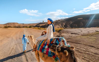 Woman riding camel in Agafay Desert, Marrakech with guide leading.