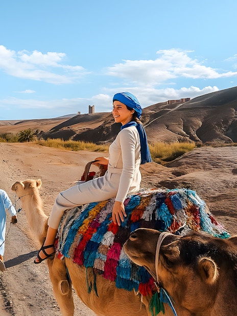 Woman riding camel in Agafay Desert, Marrakech with guide leading.