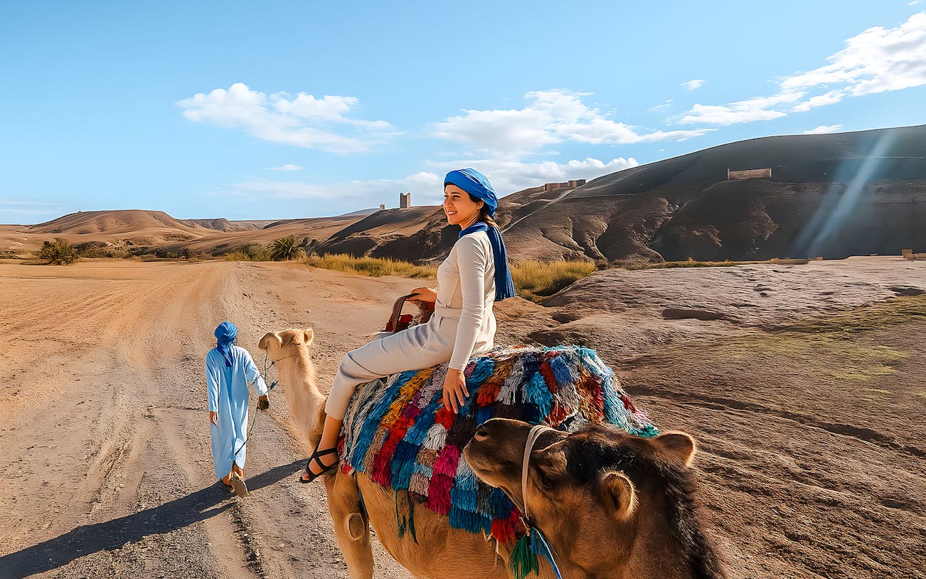 Woman riding camel in Agafay Desert, Marrakech with guide leading.