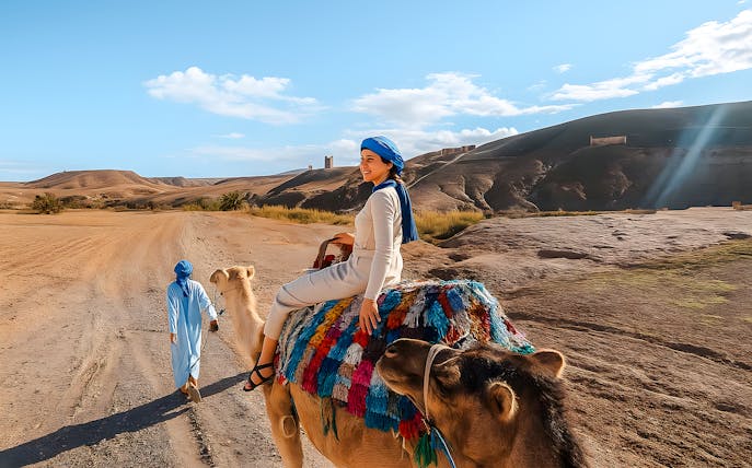Woman riding camel in Agafay Desert, Marrakech with guide leading.