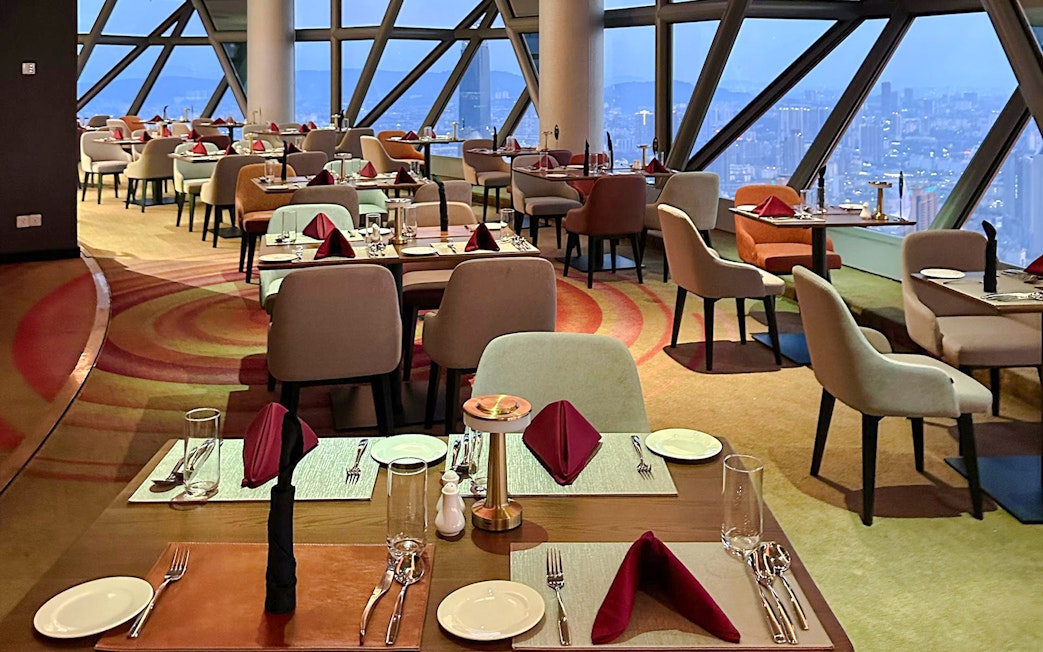 Dining area in ORBIT Revolving Restaurant with city view through large windows.
