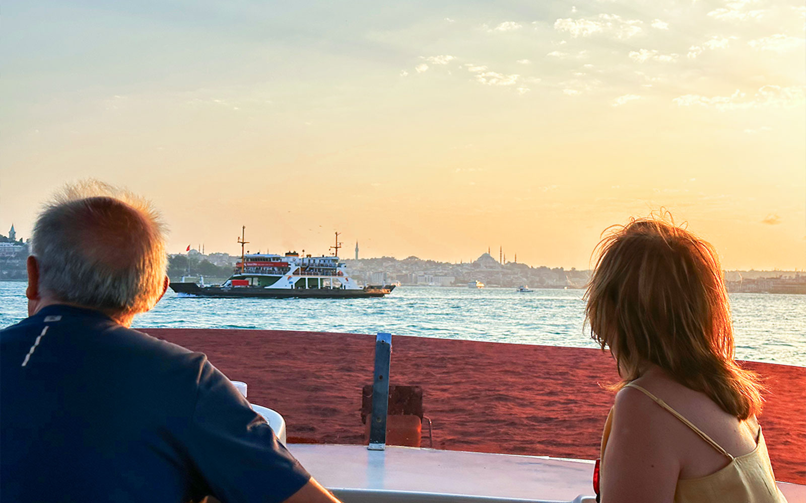 Guests enjoying Bosphorus view during sunset yacht cruise, Istanbul skyline in background.