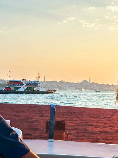 Guests enjoying Bosphorus view during sunset yacht cruise, Istanbul skyline in background.