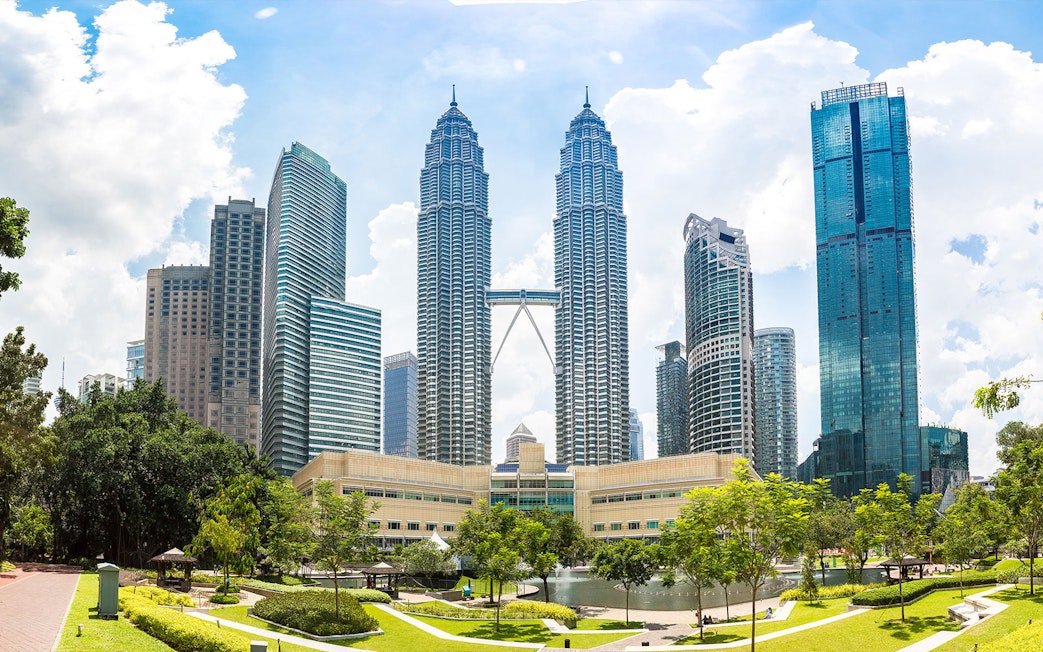 Petronas Twin Towers in Kuala Lumpur with surrounding skyscrapers and park.