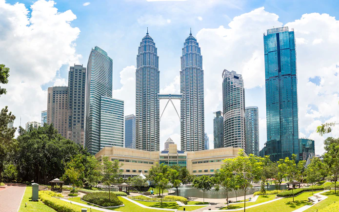Petronas Twin Towers in Kuala Lumpur with surrounding skyscrapers and park.