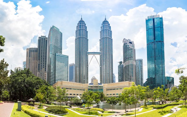 Petronas Twin Towers in Kuala Lumpur with surrounding skyscrapers and park.