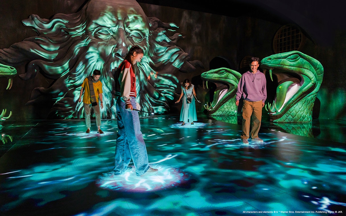 Visitors exploring Chamber of Secrets exhibit with serpent statues, Harry Potter Visions of Magic.