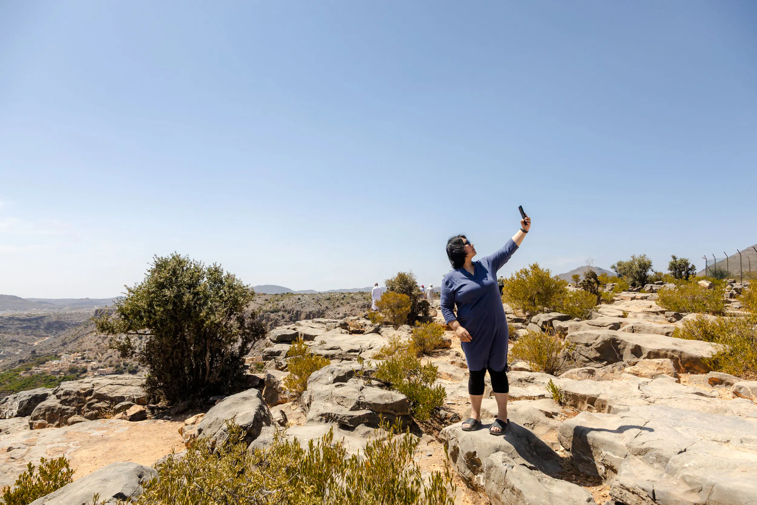 Person taking a selfie on rocky terrain at Jebel Akhdar, Oman, with scenic mountain views.
