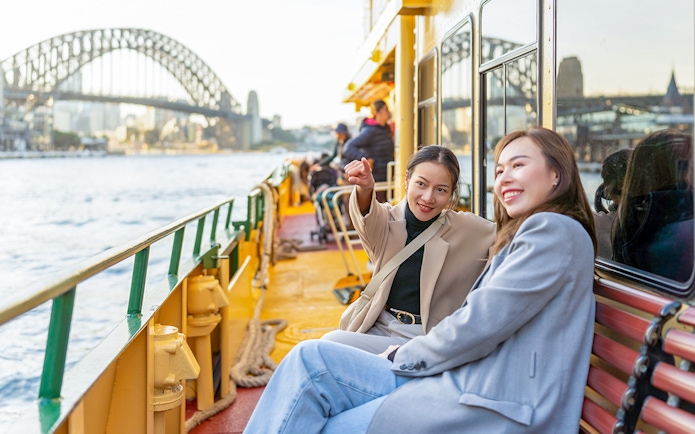 Women enjoying a ferry ride with Sydney Harbour Bridge in the background.