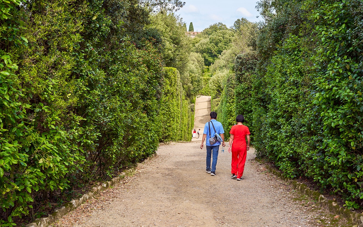Tourists walking through lush greenery in Boboli Gardens, Florence, Italy.