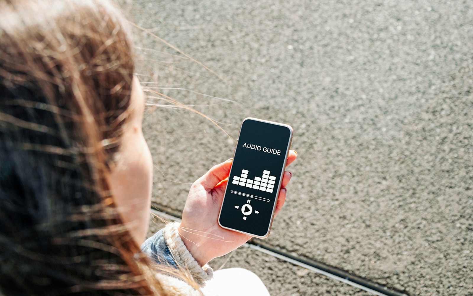 Person holding smartphone displaying audioguide app interface.