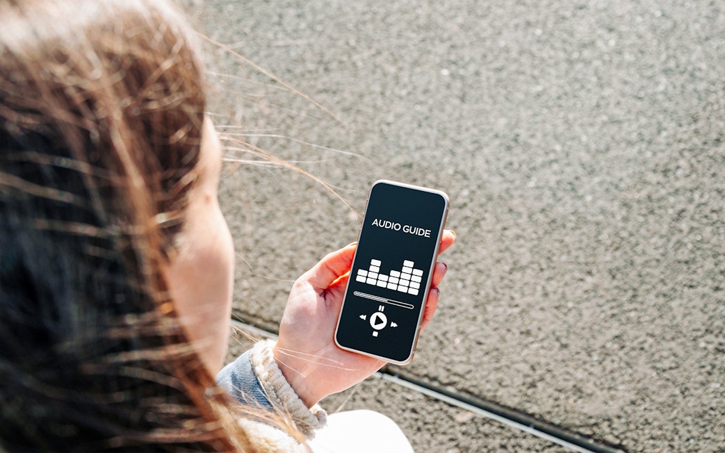 Person holding smartphone displaying audioguide app interface.