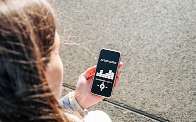Person holding smartphone displaying audioguide app interface.