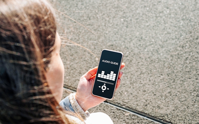 Person holding smartphone displaying audioguide app interface.