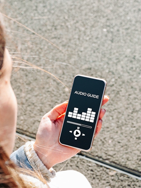 Person holding smartphone displaying audioguide app interface.