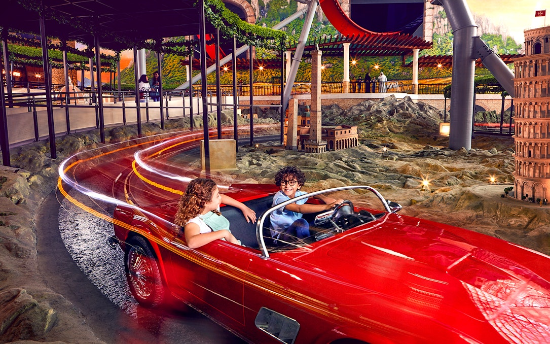 Visitors enjoying a ride in a red car at Ferrari World Abu Dhabi, with miniature landmarks in view.
