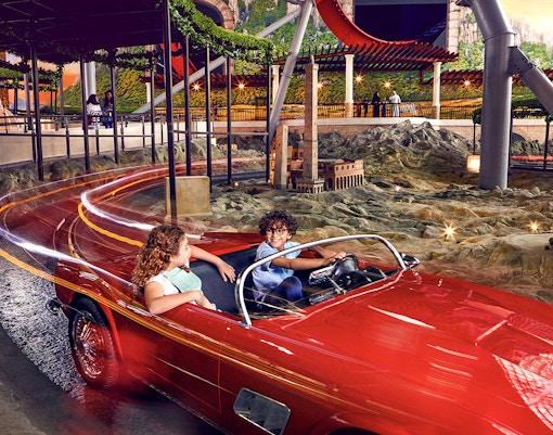 Visitors enjoying a ride in a red car at Ferrari World Abu Dhabi, with miniature landmarks in view.