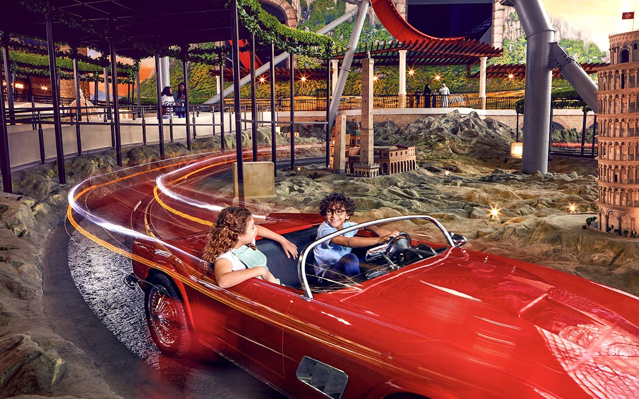 Visitors enjoying a ride in a red car at Ferrari World Abu Dhabi, with miniature landmarks in view.