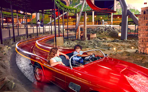 Visitors enjoying a ride in a red car at Ferrari World Abu Dhabi, with miniature landmarks in view.
