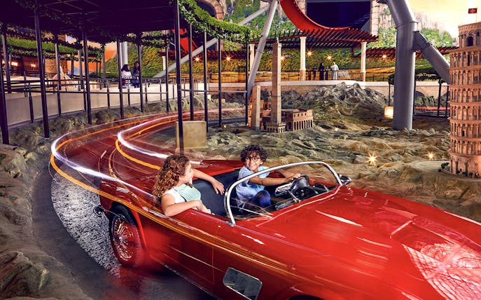 Visitors enjoying a ride in a red car at Ferrari World Abu Dhabi, with miniature landmarks in view.