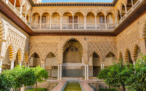 Courtyard of Alcazar Seville with intricate arches and lush greenery.