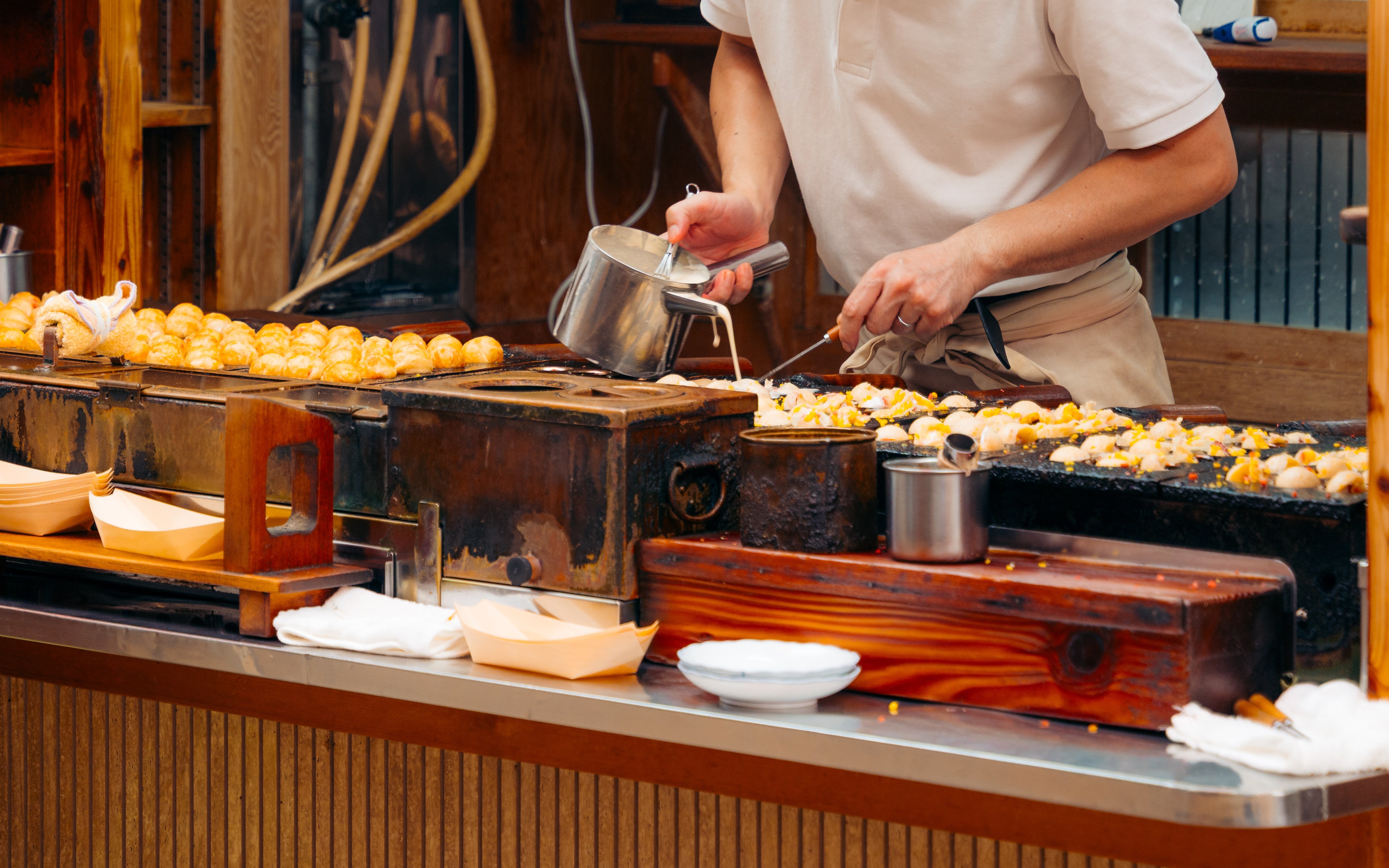 Osaka chef cooking takoyaki on a grill at a street food stall.