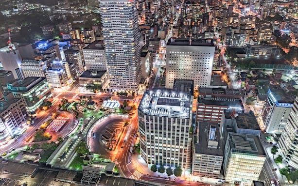Aerial view of illuminated cityscape in Japan at night, showcasing bustling streets and skyscrapers.