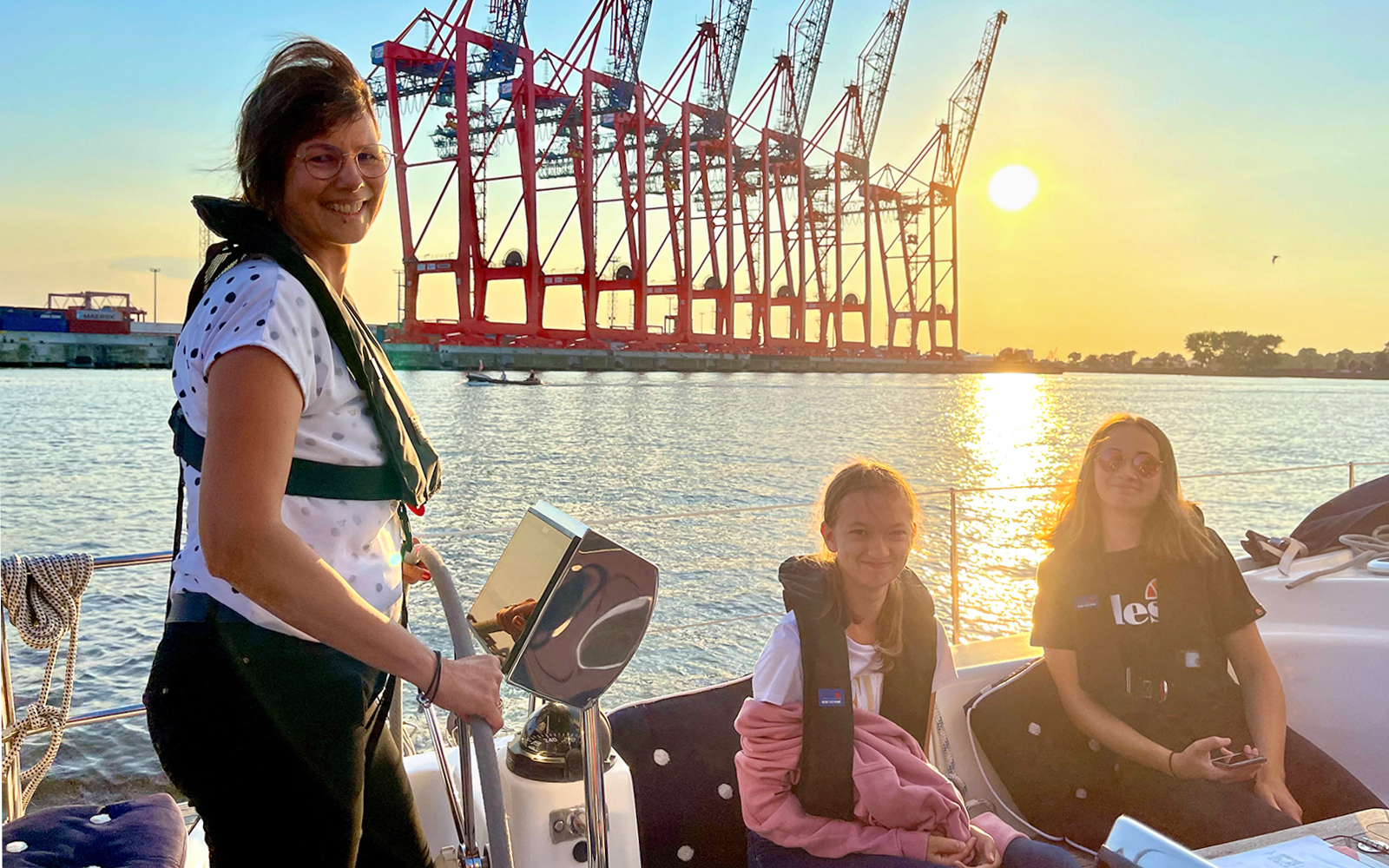 Sailing tour in the Port of Hamburg with cranes in the sunset background.