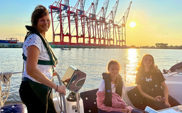 Sailing tour in the Port of Hamburg with cranes in the sunset background.