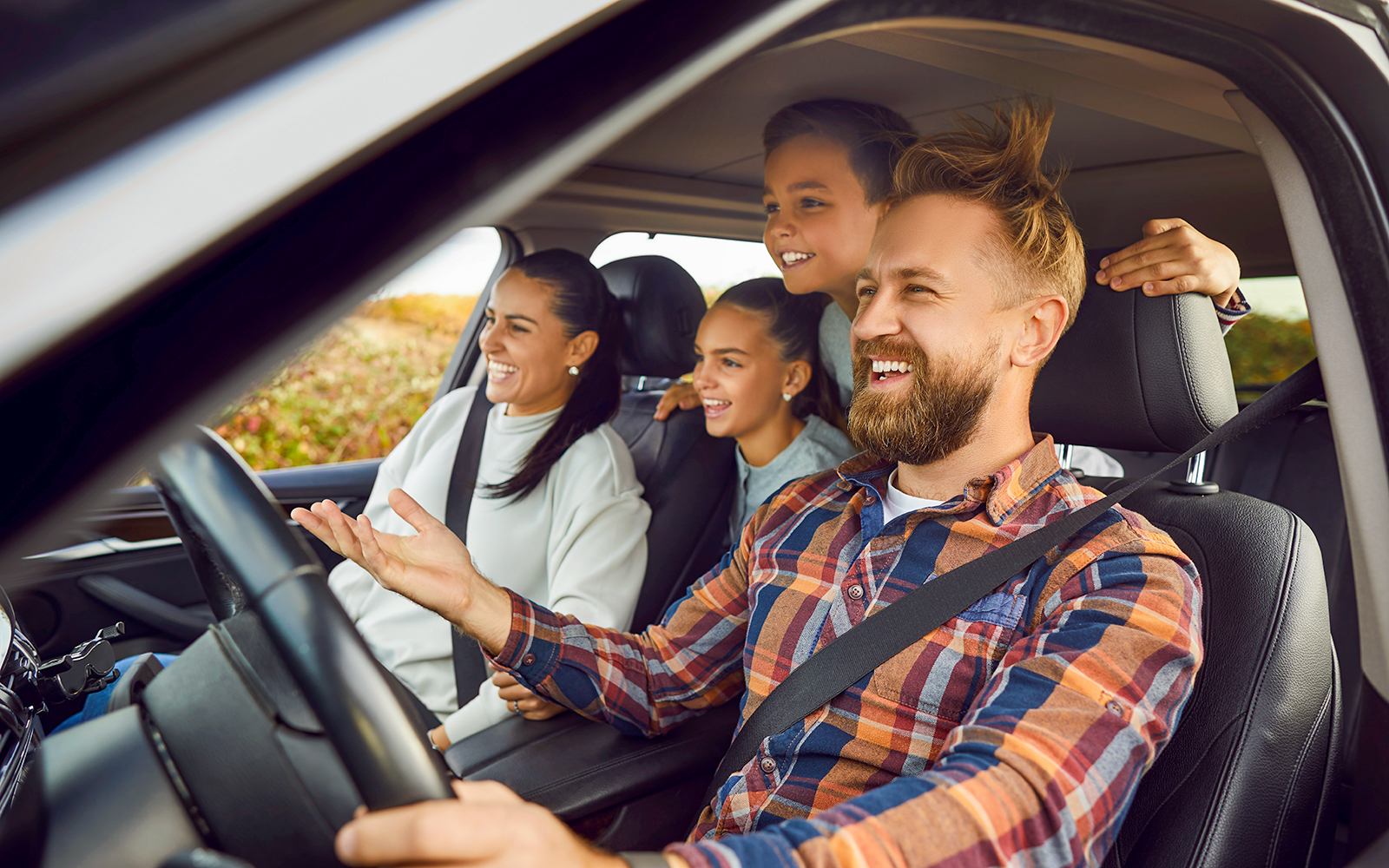 Family enjoying a road trip in a car, smiling and looking out the window.