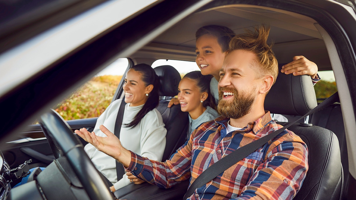 Family enjoying a road trip in a car, smiling and looking out the window.