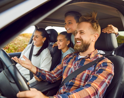 Family enjoying a road trip in a car, smiling and looking out the window.