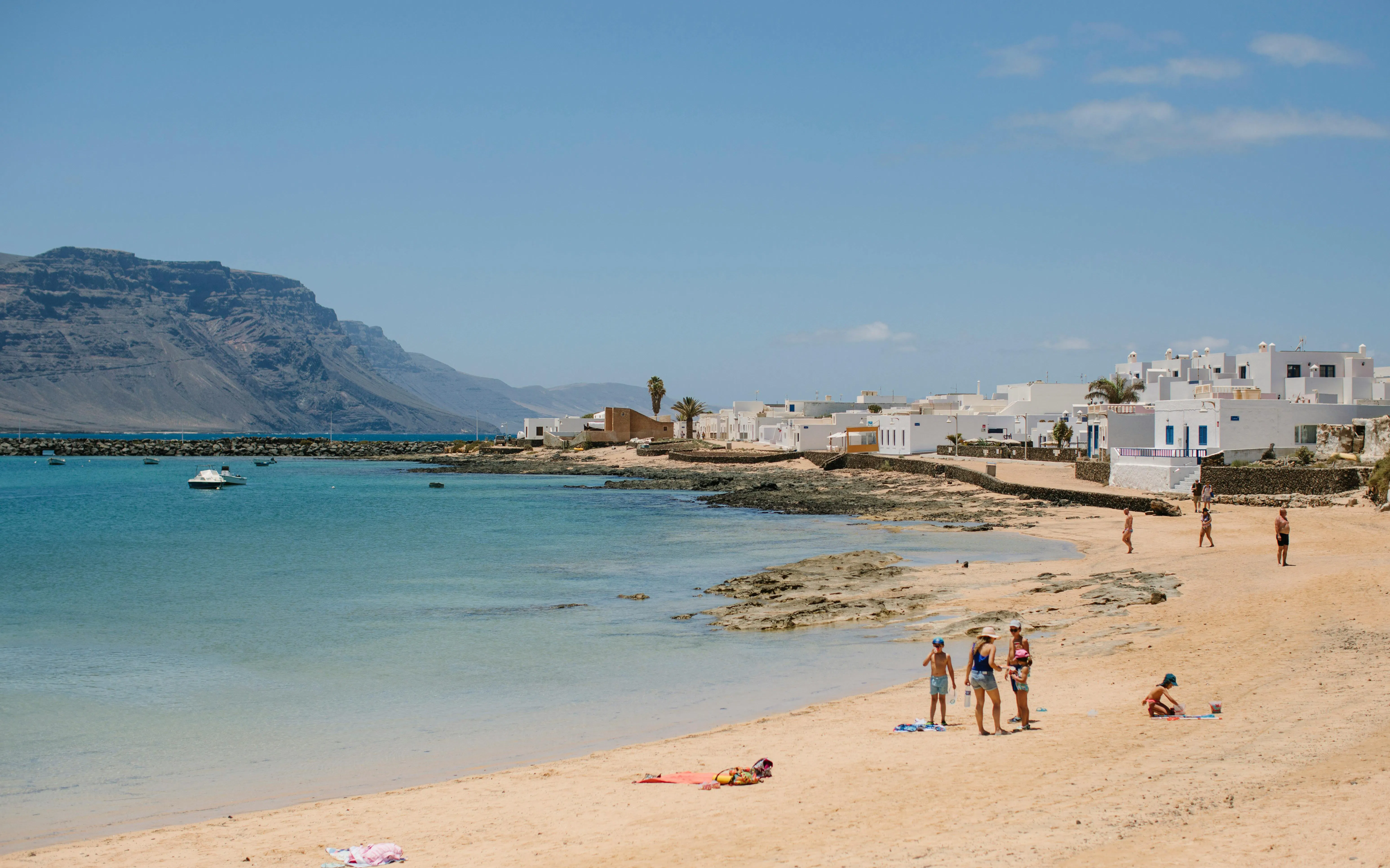 Beachgoers on Playa de Caleta del Sebo, La Graciosa, Canary Islands, with white buildings and mountains.