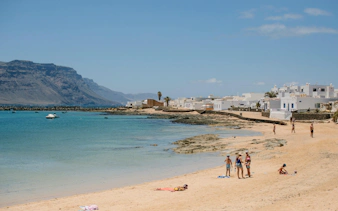 Beachgoers on Playa de Caleta del Sebo, La Graciosa, Canary Islands, with white buildings and mountains.